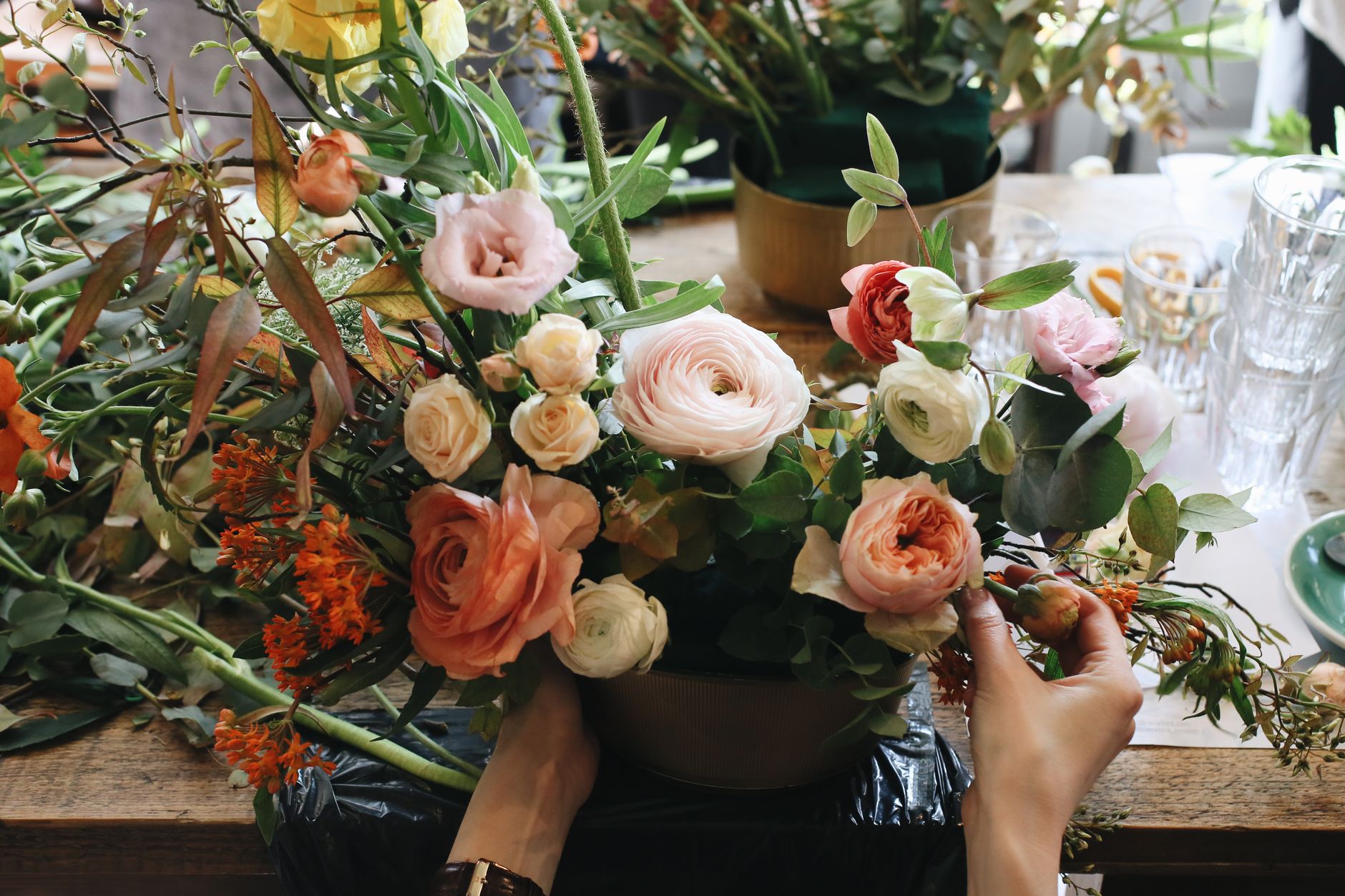 Hands arranging a representative bouquet of peach, pink, and white flowers